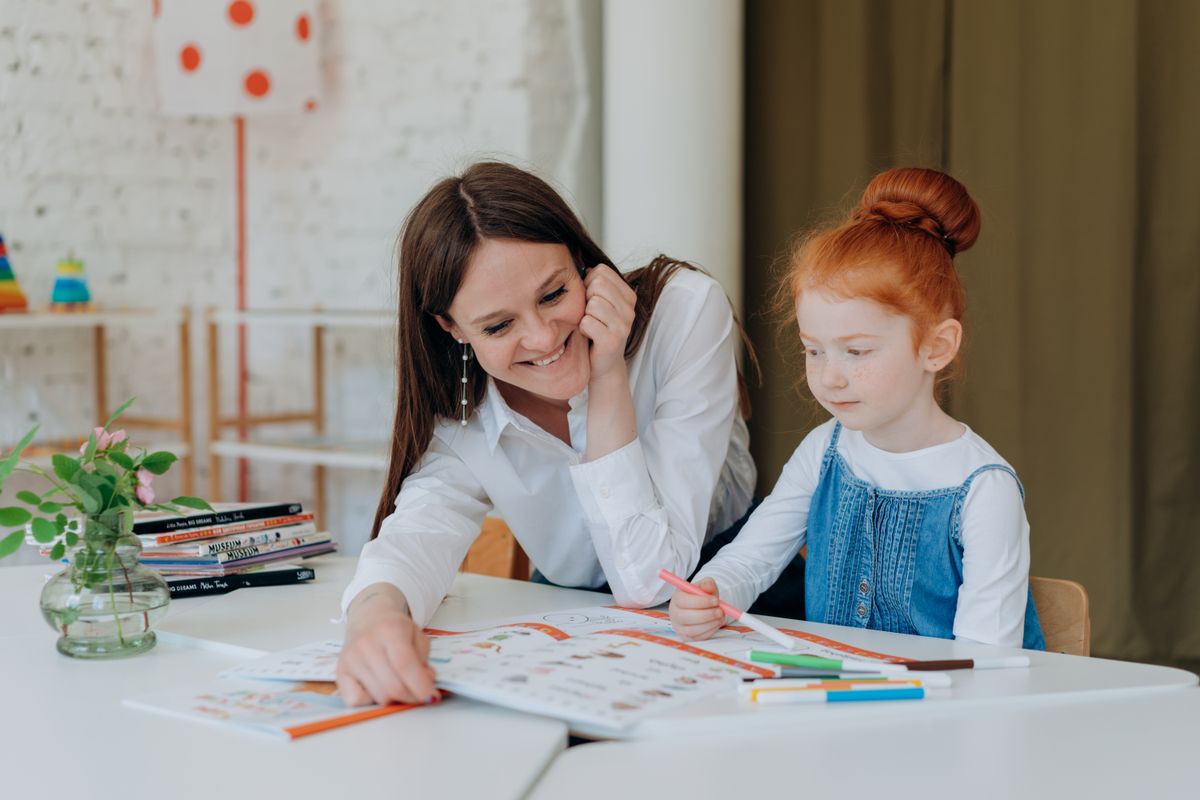 Special educationist guiding a child through a reading and writing exercise at a home table